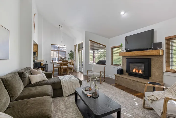 Living area featuring a stone-clad fireplace with wood mantle, vaulted ceilings, and wood-finish flooring