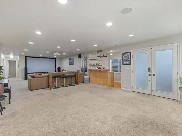 Expansive entertainment space featuring recessed lighting, a large projection screen, and a wet bar with built-in shelving