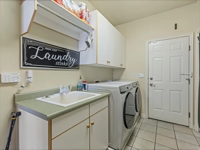 Dedicated laundry area featuring a utility sink with a laminate countertop, built-in upper and lower cabinetry, and tiled flooring