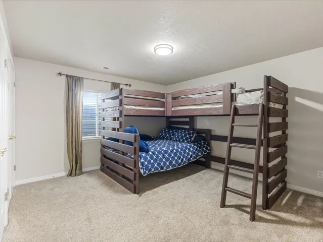 Bedroom #5 featuring a window with blinds and curtains, a ceiling-mounted light fixture, and two white bi-fold doors with brass hardware