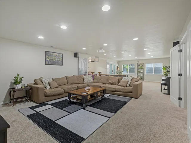 Spacious living area featuring neutral carpeting, recessed ceiling lighting, and multiple windows with horizontal blinds