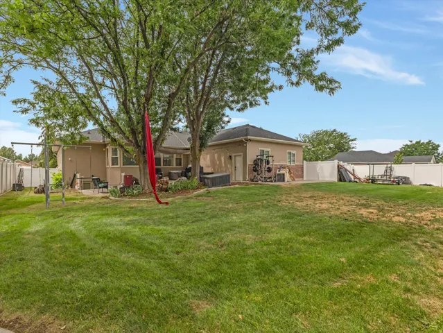 Expansive rear yard featuring mature trees, a concrete patio, a stucco-clad exterior, and a detached structure with a pitched roof