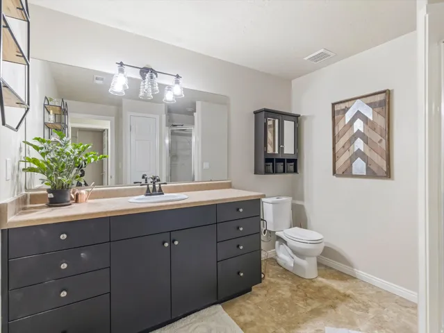 Spacious bathroom featuring an extended dark wood-finish vanity with a single basin sink, a large wall-mounted mirror, and a contemporary four-light fixture