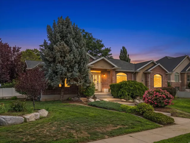 Brick and stucco exterior featuring arched windows, mature landscaping, a manicured lawn, and a paved walkway