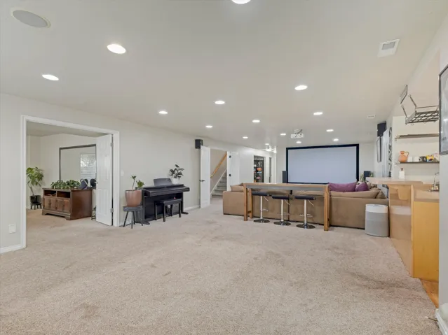 Spacious entertainment room featuring recessed lighting, a large projection screen, and an integrated bar area