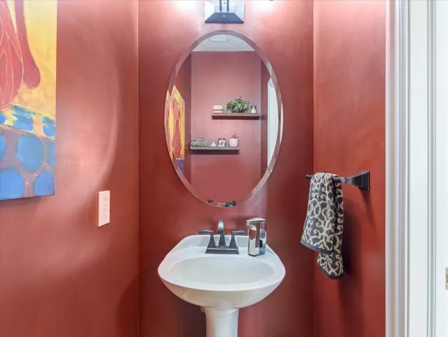 Half bathroom with pedestal sink, dark-toned fixtures and an oval mirror
