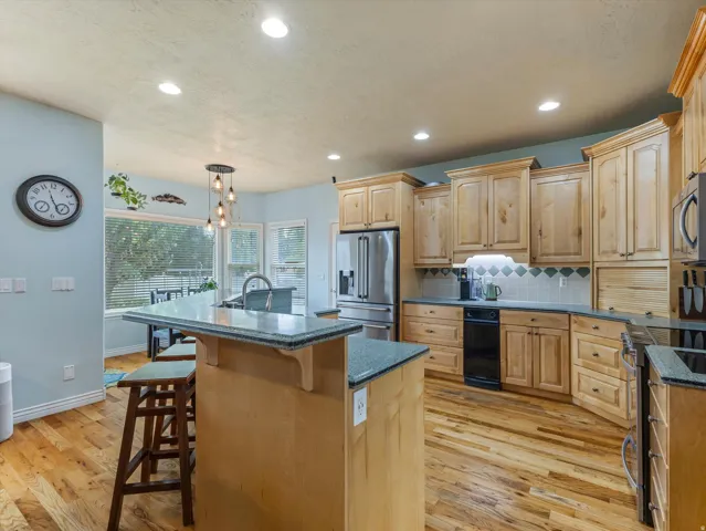 Kitchen featuring wood-finish flooring, light wood cabinetry, stone countertops, a large center island with seating, and stainless steel appliances