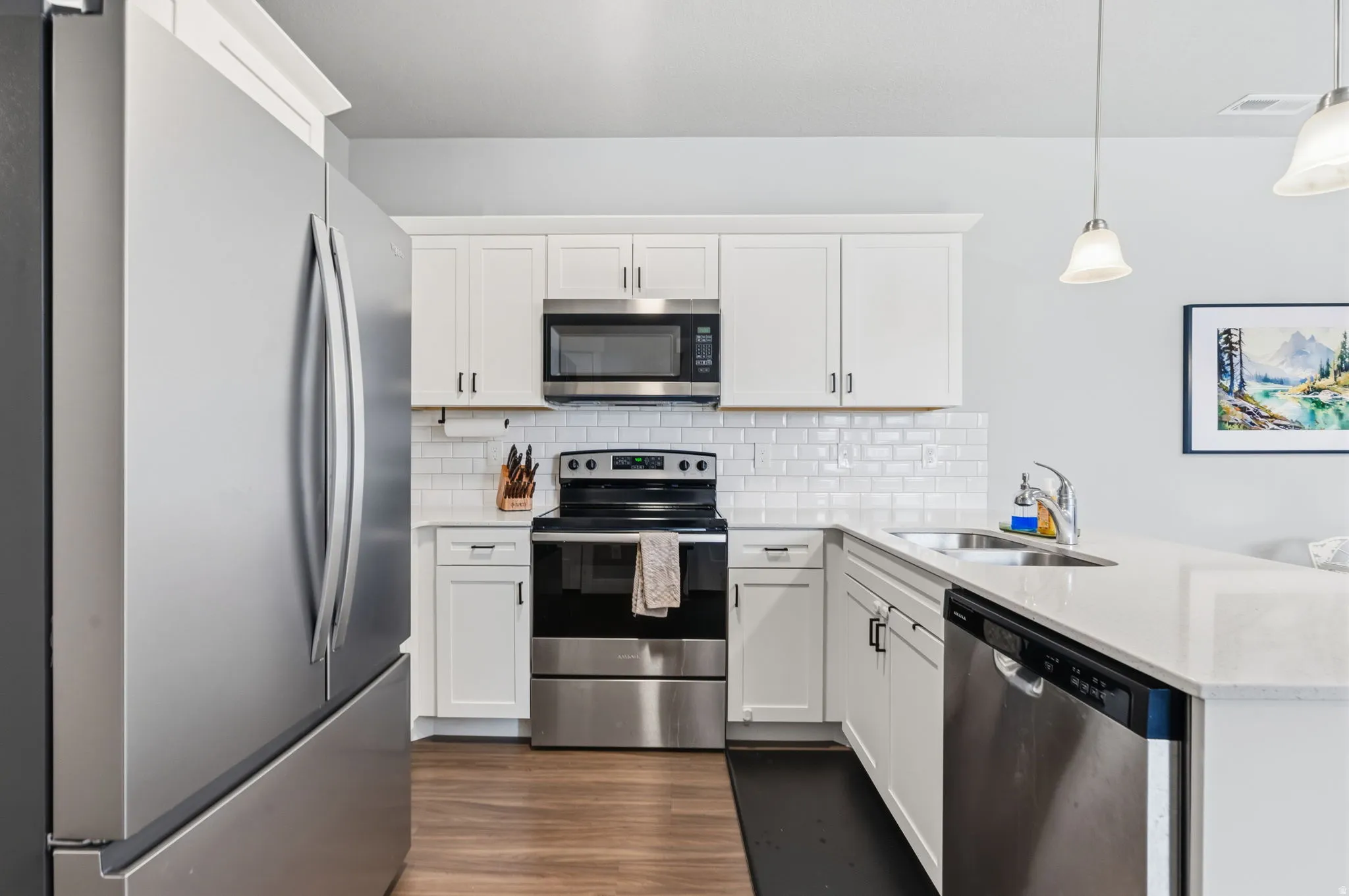 Kitchen featuring stainless steel appliances, white cabinetry, subway tile backsplash, wood-finish flooring, and pendant lighting