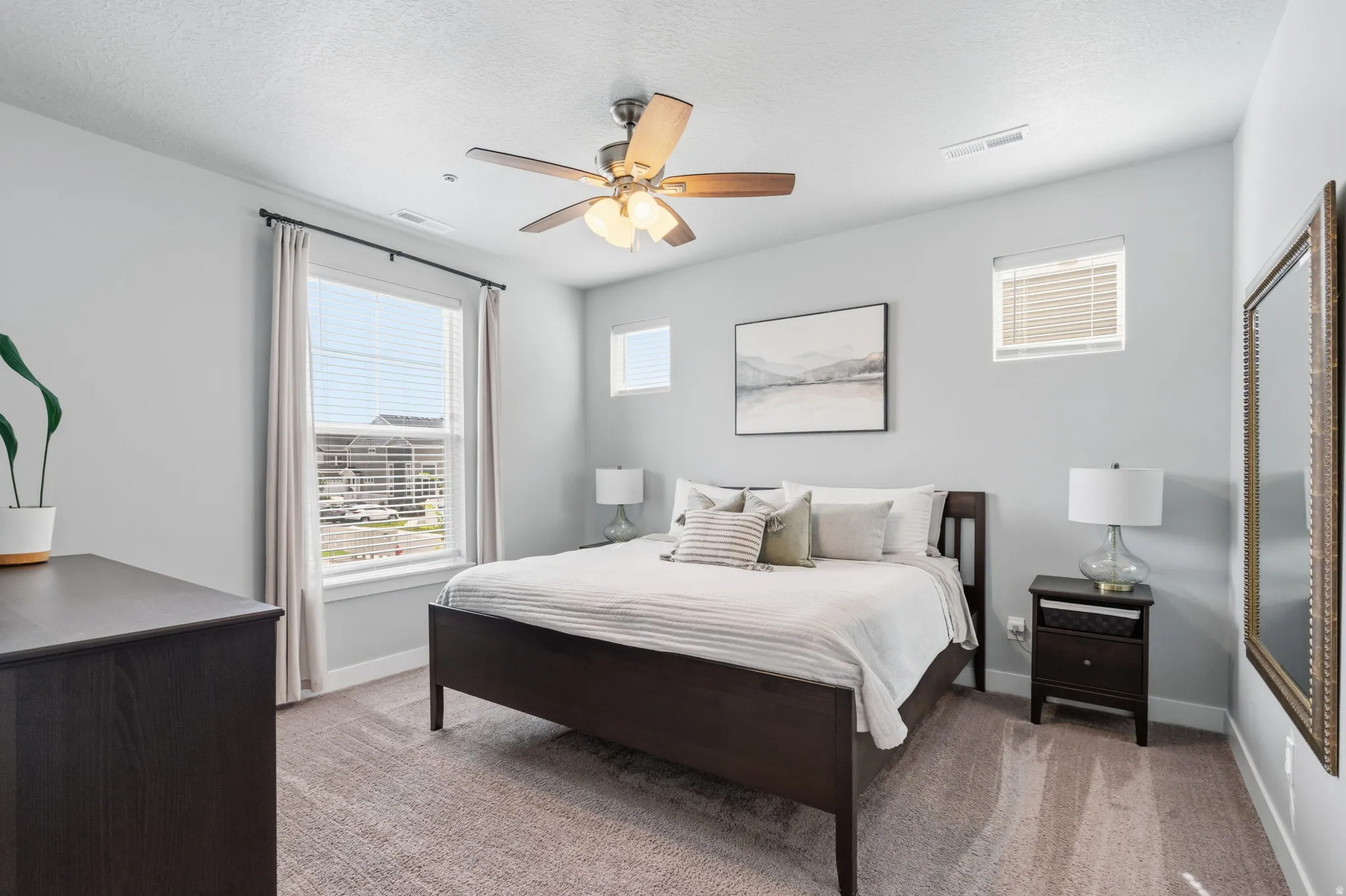 Bedroom featuring light gray walls, plush carpet flooring, a ceiling fan with integrated lighting, and multiple windows with blinds for natural light