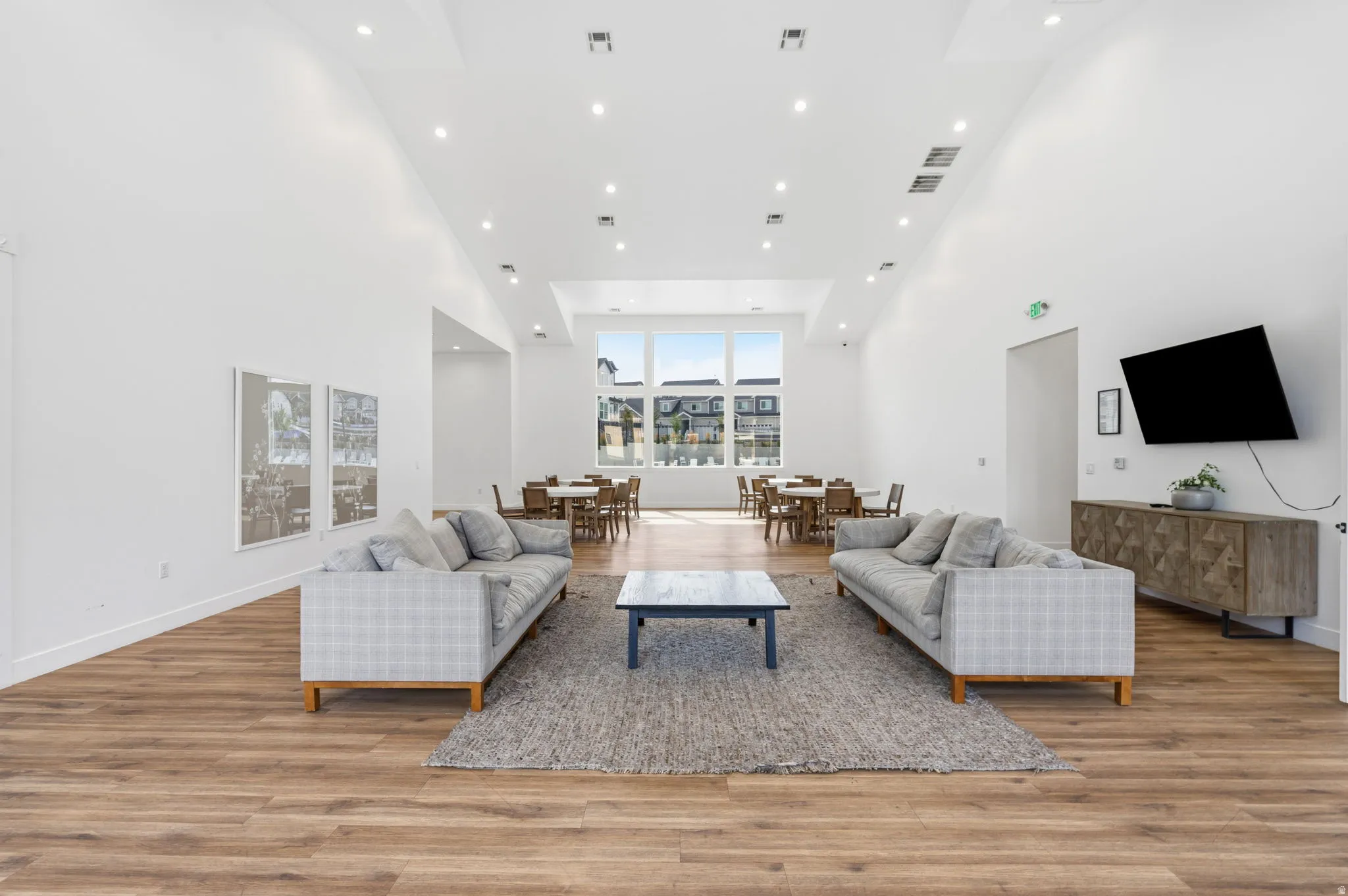 Spacious common area featuring wood-finish flooring, high vaulted ceilings with recessed lighting, and large windows providing abundant natural light