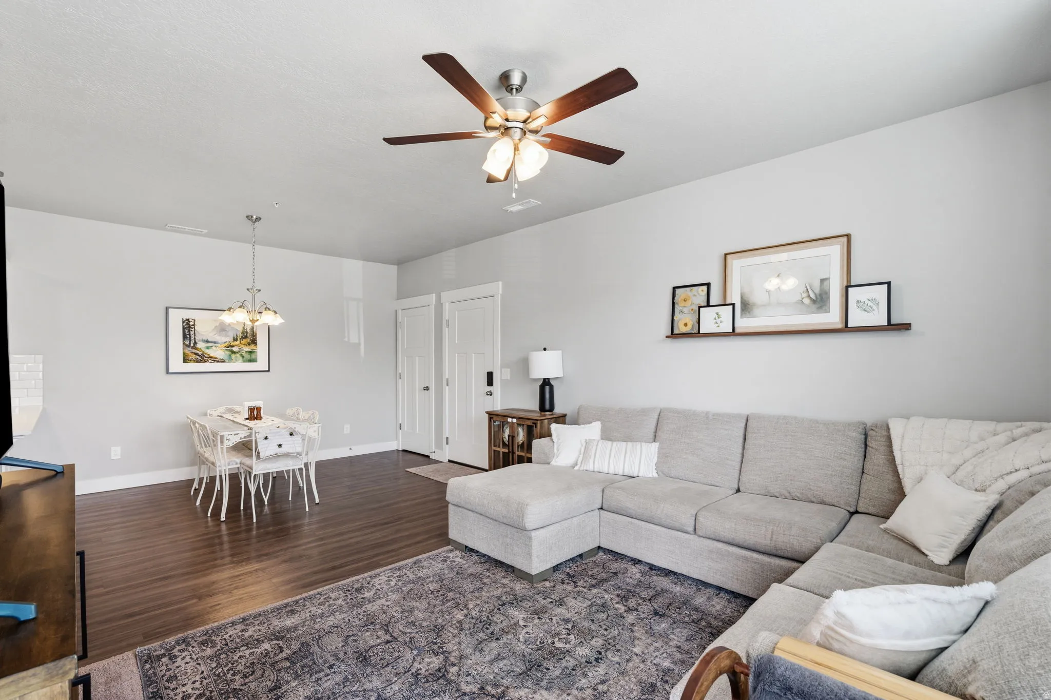 Open-concept living area featuring wood-finish flooring, a ceiling fan with light fixture, and a dining area with a chandelier