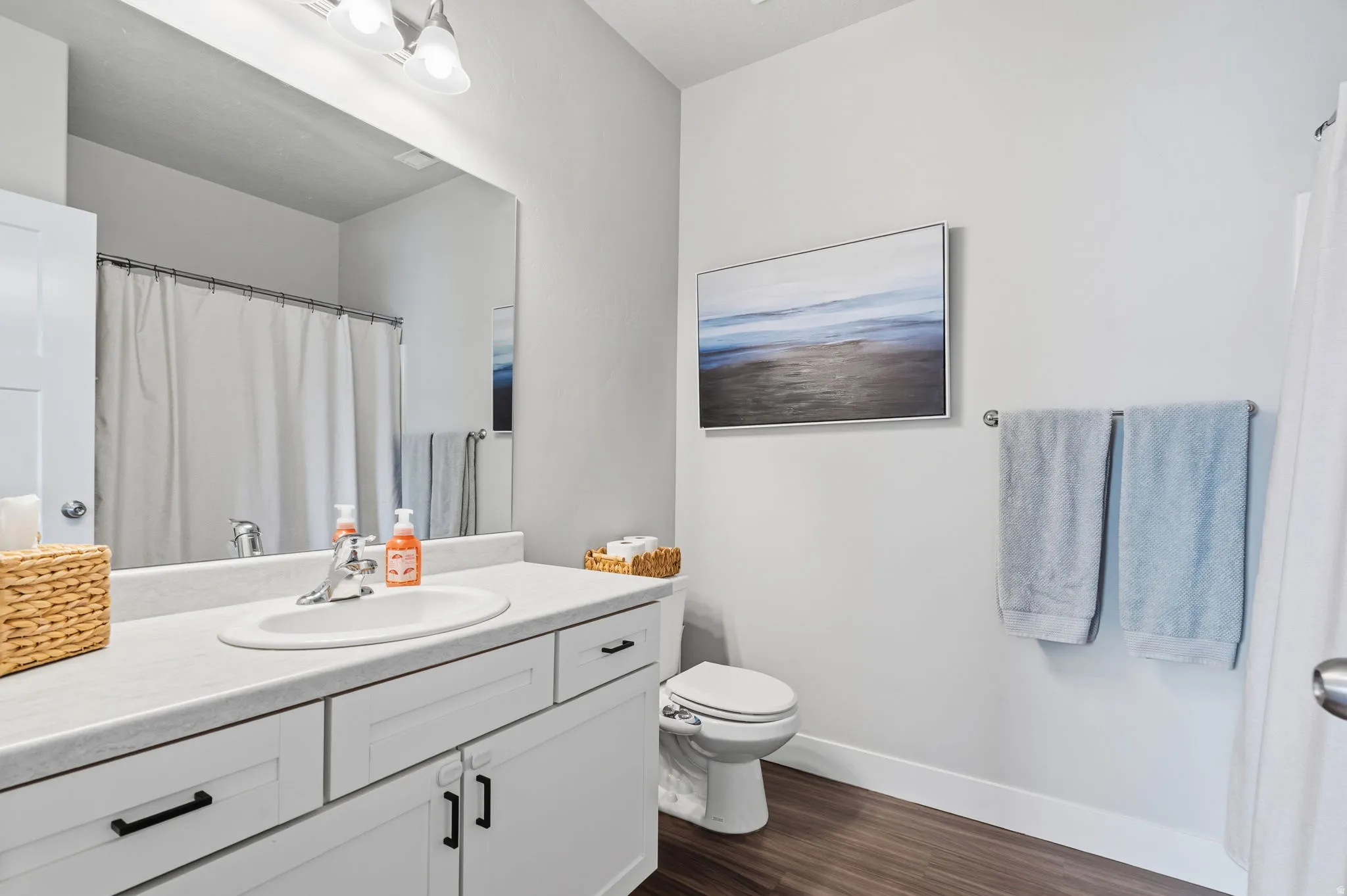 Bathroom featuring a single vanity with a white countertop, undermount sink, and white cabinetry with black hardware