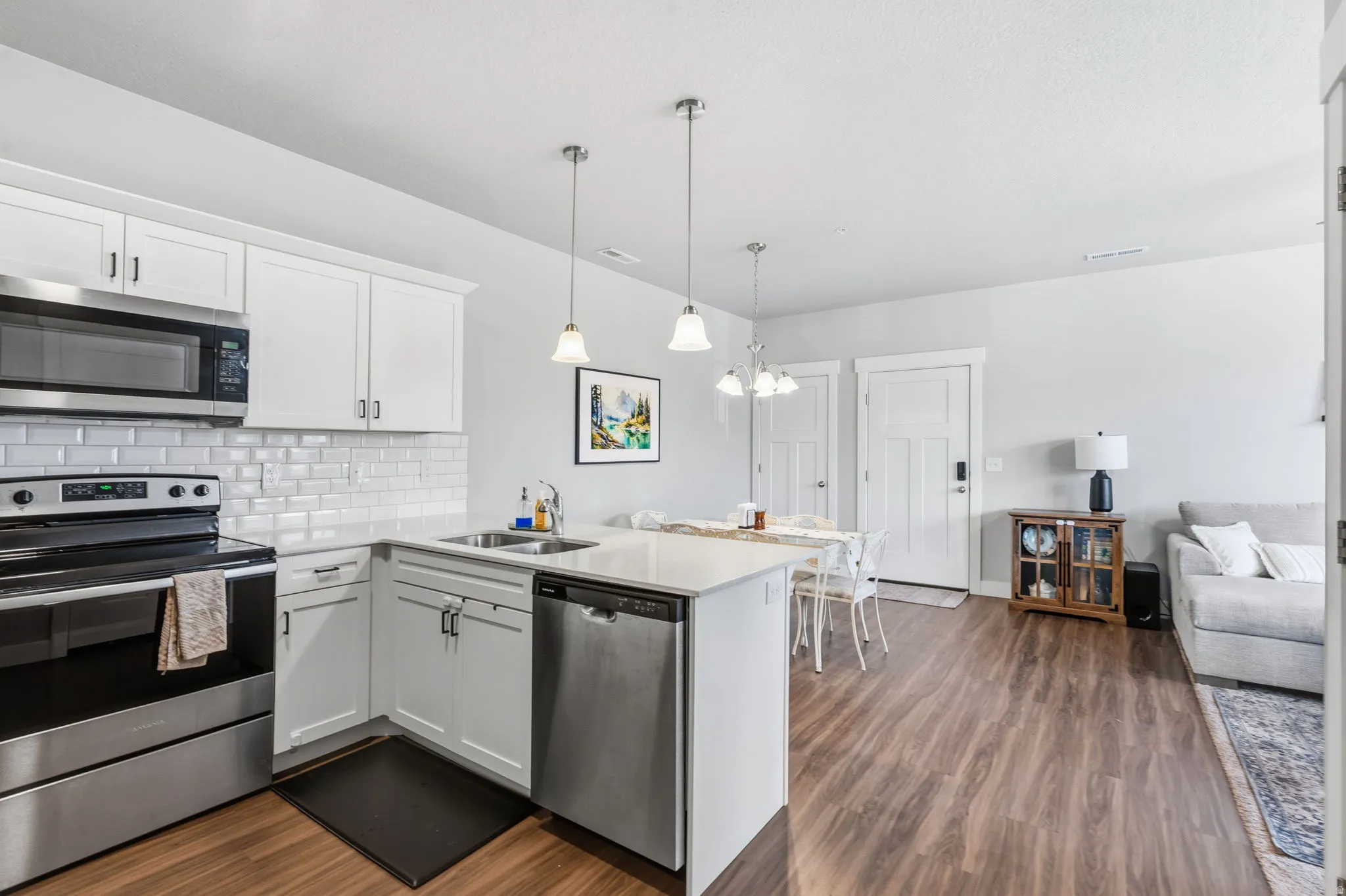 Kitchen featuring white shaker cabinetry, stainless steel appliances, white subway tile backsplash, and light-toned countertops