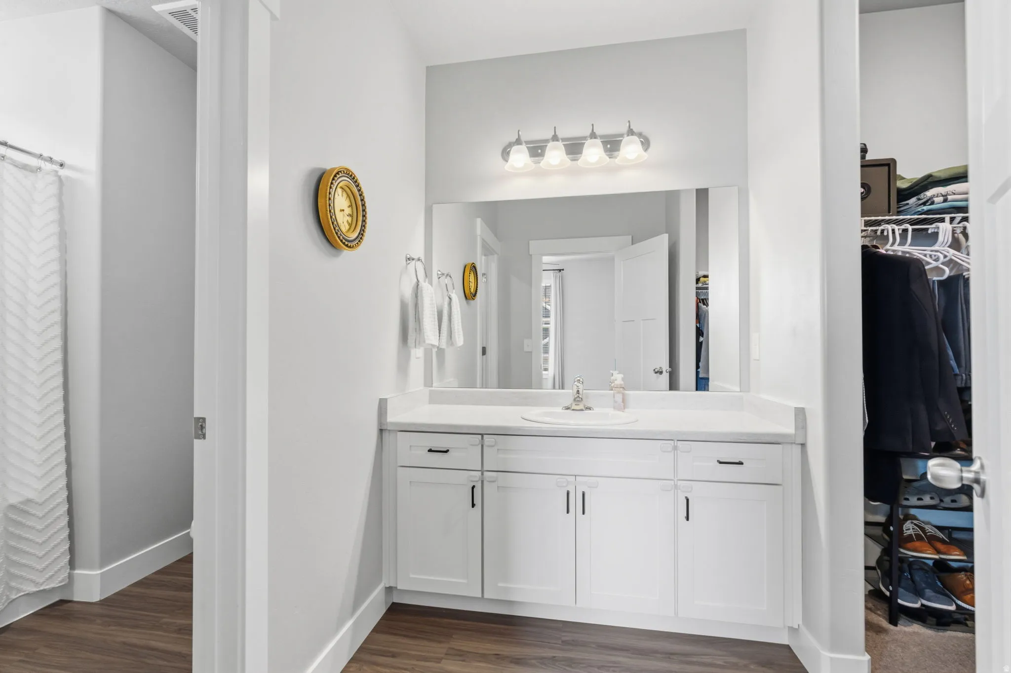 Bathroom vanity featuring a single basin sink, white cabinetry with dark hardware, and a large mirror