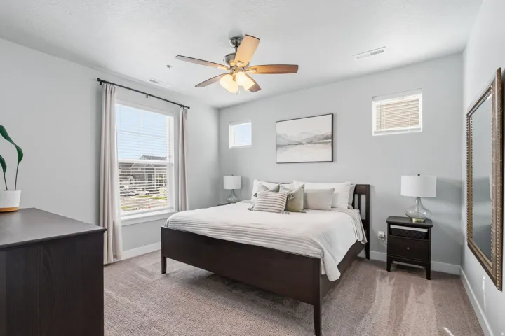 Bedroom featuring light gray walls, plush carpet flooring, a ceiling fan with integrated lighting, and multiple windows with blinds for natural light