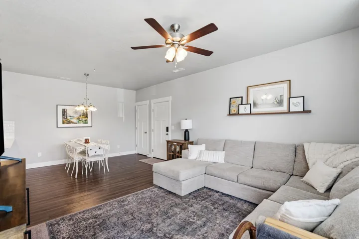Open-concept living area featuring wood-finish flooring, a ceiling fan with light fixture, and a dining area with a chandelier