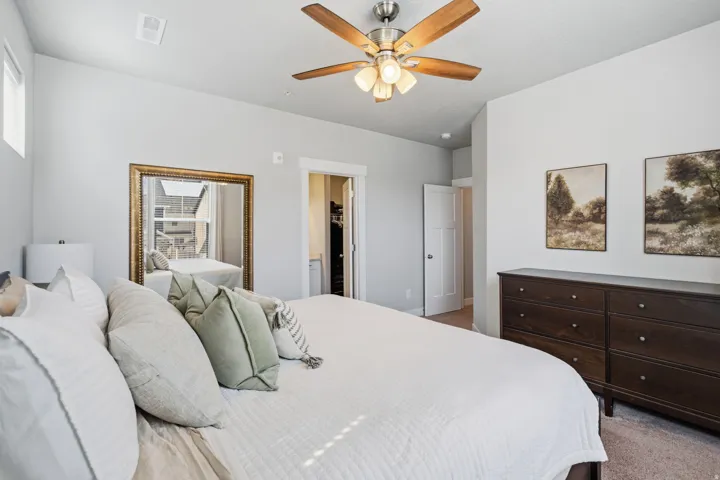 Spacious bedroom featuring light neutral wall paint, a built-in ceiling fan with integrated lighting, and a large mirror with a gold-tone frame