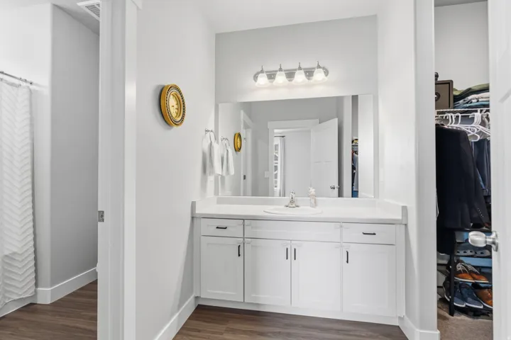 Bathroom vanity featuring a single basin sink, white cabinetry with dark hardware, and a large mirror