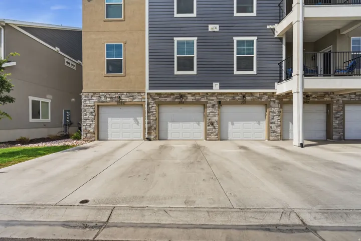 Multi-story residential facade featuring three individual garage doors, stone veneer accents, and horizontal siding