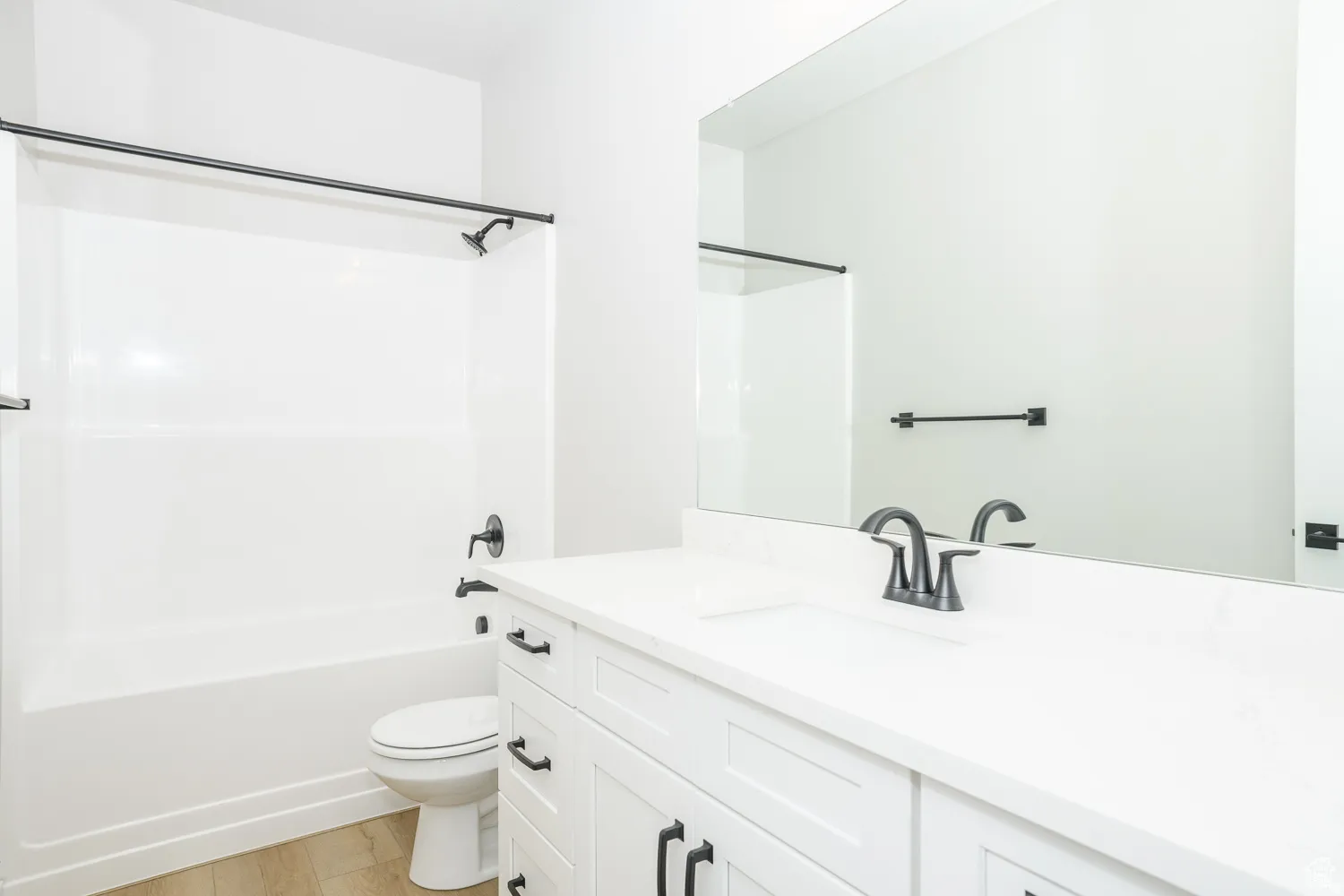Modern bathroom featuring a white vanity with shaker-style cabinetry, a white countertop with an integrated sink, a large wall-mounted mirror, and a white tub/shower combination with matte black fixtures