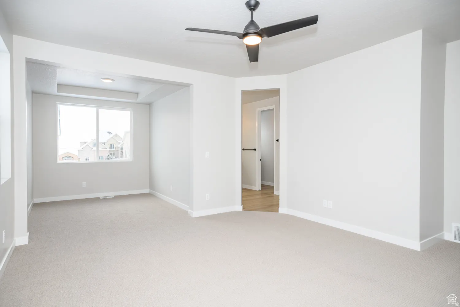 Spacious room featuring neutral carpet flooring, light gray wall tones, and a modern ceiling fan with integrated lighting