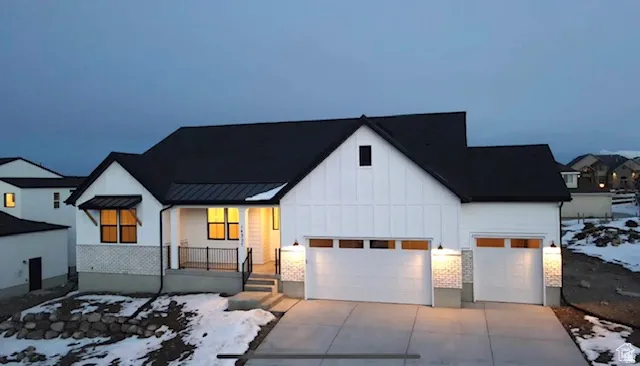 Modern farmhouse-style exterior featuring white board and batten siding, dark-framed windows, a covered front porch, and an attached two-car garage