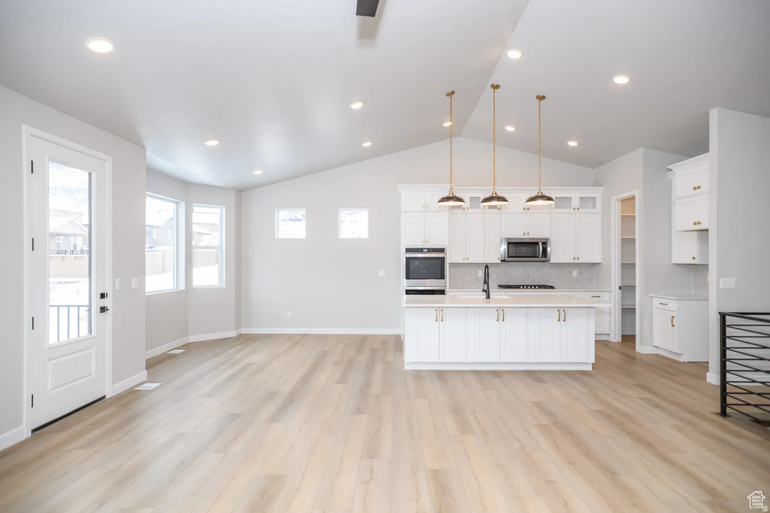 Open-concept living space featuring wood-finish flooring and a vaulted ceiling with recessed lighting