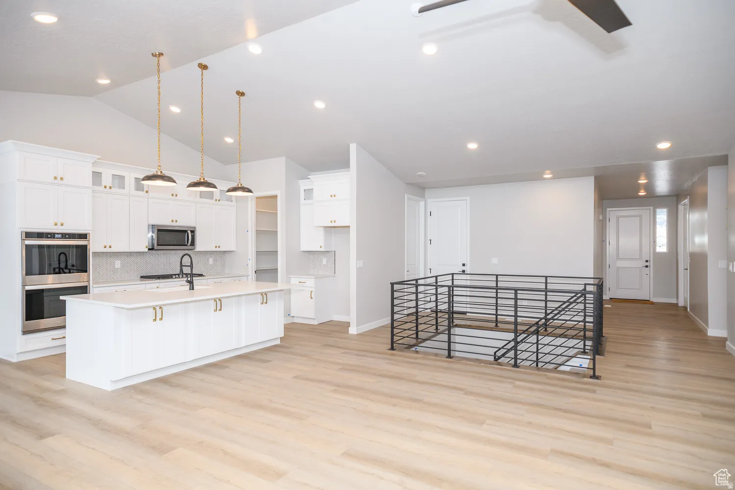 Kitchen featuring white cabinetry, a large central island with pendant lighting, stainless steel double ovens, and wood-finish flooring
