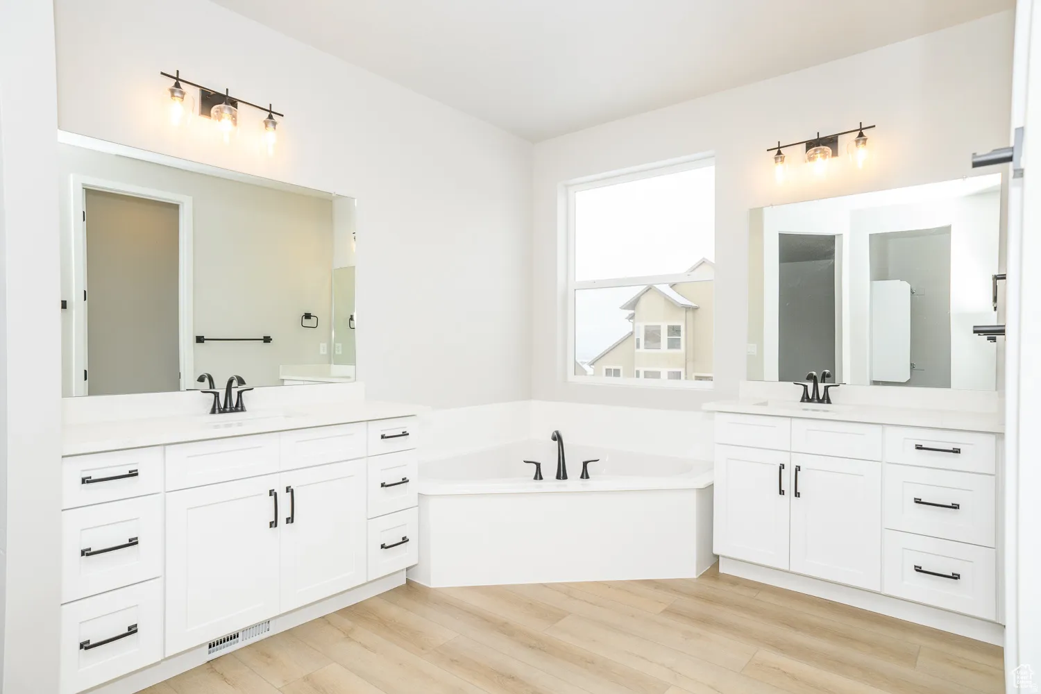 Bathroom featuring a corner soaking tub, dual vanity with white cabinetry, and wood-finish flooring