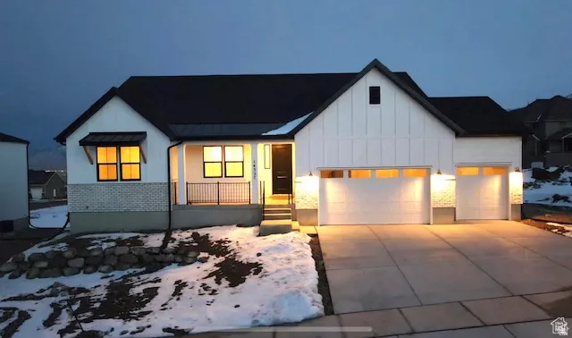 Modern farmhouse exterior featuring white board and batten siding, a black metal roof, a covered front porch with black railings, a two-car garage with upper window panels, and a concrete driveway