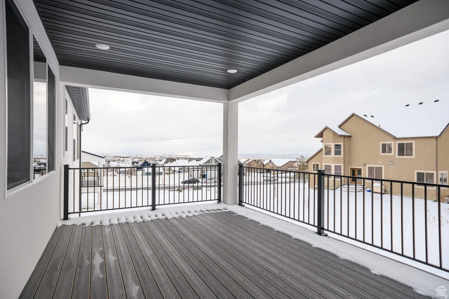 Covered outdoor deck featuring composite decking, black metal railings, and an overhead lighting fixture