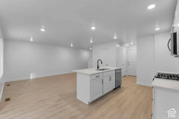 Open-concept living area featuring a kitchen island with sink, stainless steel dishwasher, gas cooktop, and wood-finish flooring
