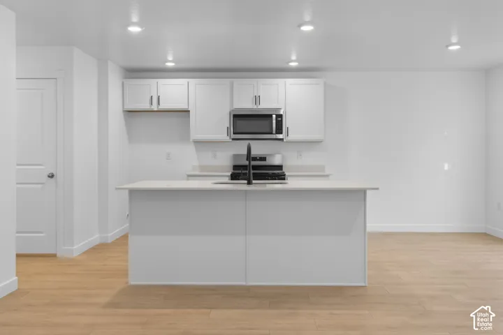 Kitchen featuring white cabinetry, stainless steel microwave, black range, and an island with a light-colored countertop