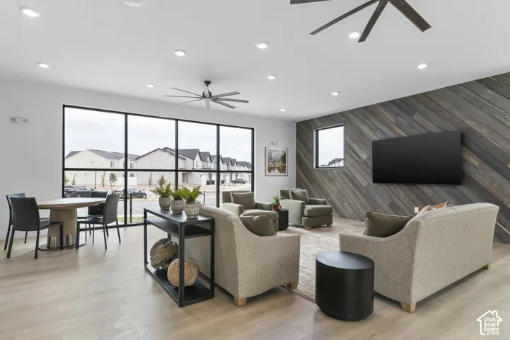 Spacious common area featuring light wood-finish flooring, a full wall of black-framed windows, recessed lighting, and modern ceiling fans