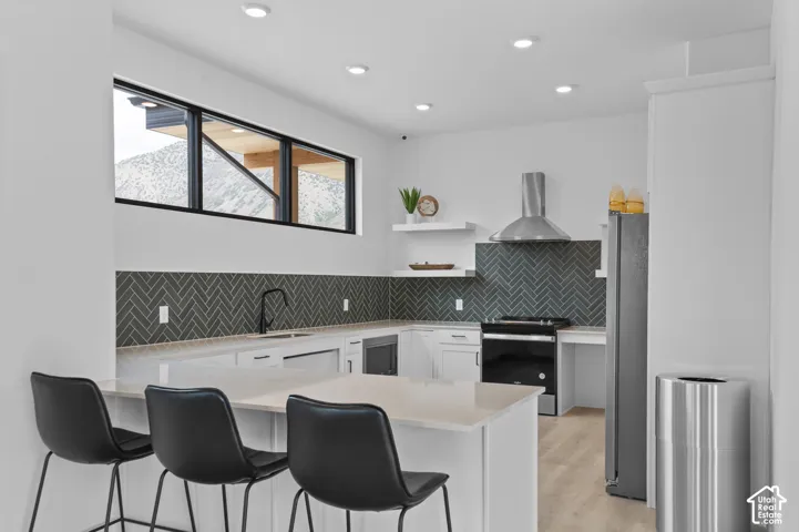 Contemporary kitchen featuring a herringbone tile backsplash, white cabinetry, integrated stainless steel appliances, a bar-height countertop, and a built-in kitchen island