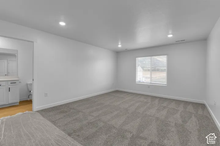 Spacious room featuring neutral carpeting, white walls, recessed lighting, and a window with blinds