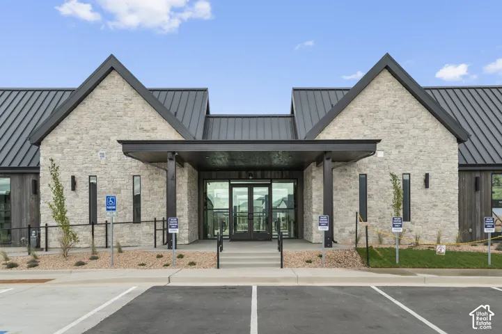 Contemporary architectural design featuring a stone and wood facade, a prominent metal roof, and a covered entry with large glass doors