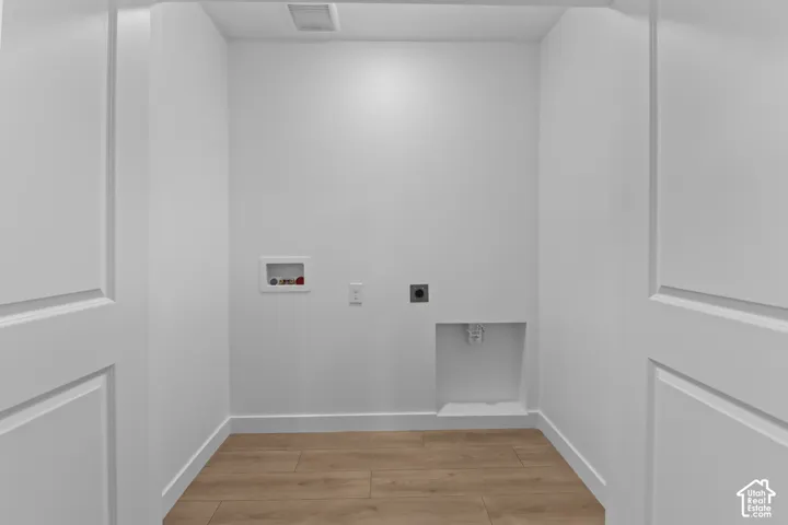 Dedicated laundry area featuring wood-finish flooring, crisp white walls, and a recessed dryer vent