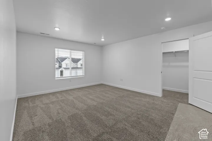 Spacious room featuring neutral carpeting, a large window with horizontal blinds, recessed lighting, and a closet with a bi-fold door