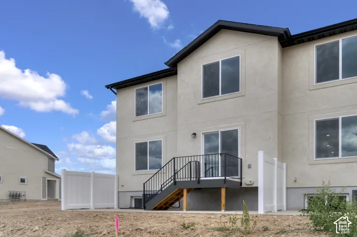 Rear exterior featuring a two-story stucco facade, multiple large windows, a sliding glass door, a deck with black metal railings, and a white privacy fence
