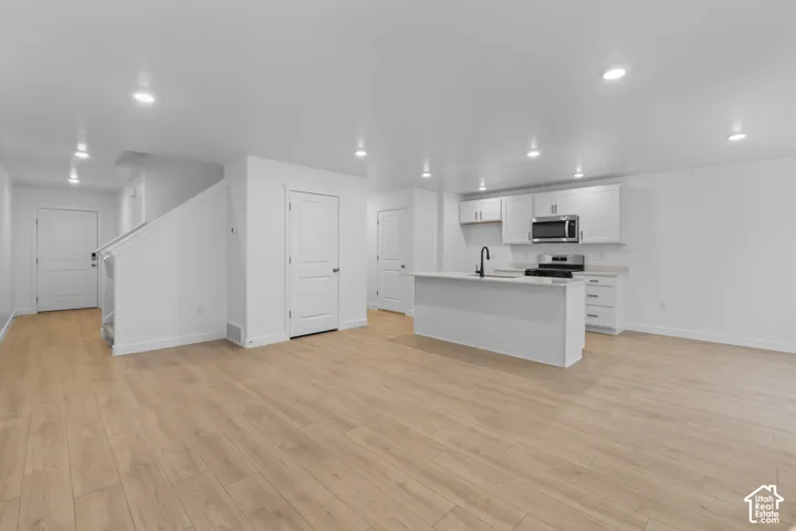 Open-concept living space featuring wood-finish flooring, recessed lighting, and a white kitchen with an island, stainless steel appliances, and a matte black faucet