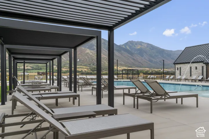 Expansive outdoor pool area featuring a stone-clad building with a dark metal roof, a rectangular swimming pool, and multiple sun loungers