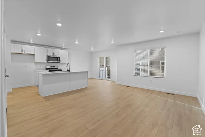 Open-concept living space featuring wood-finish flooring, recessed lighting, and a white kitchen with an island, stainless steel appliances, and white cabinetry