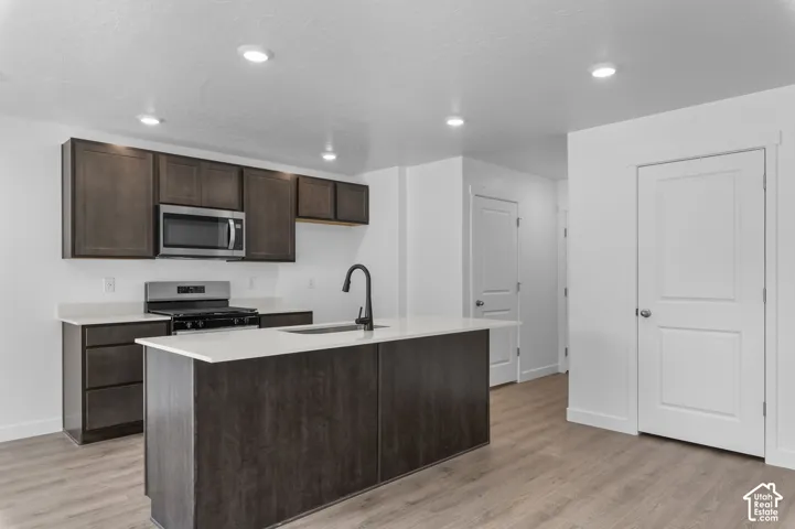 Modern kitchen featuring dark wood-finish cabinetry, light countertops, and a central island with an undermount sink and black faucet