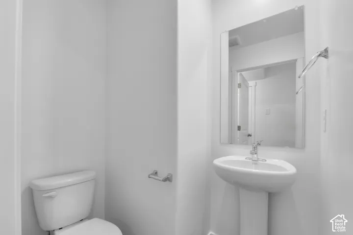 Pedestal sink with chrome faucet, wall-mounted mirror, white toilet, and chrome toilet paper holder