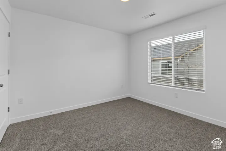 Neutral color palette featuring a window with horizontal blinds, textured carpet flooring, and white baseboards