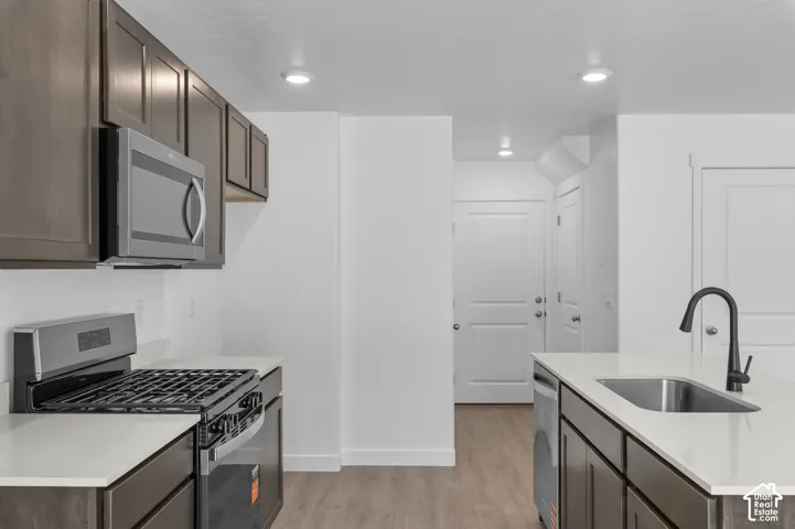 Contemporary kitchen featuring dark wood cabinetry, light countertops, stainless steel appliances, and wood-finish flooring