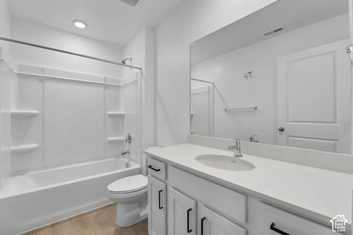 Bathroom featuring a white tub/shower combination, light wood-finish flooring, a vanity with white cabinetry and black hardware, a white countertop with an integrated sink, and a large wall-mounted mirror