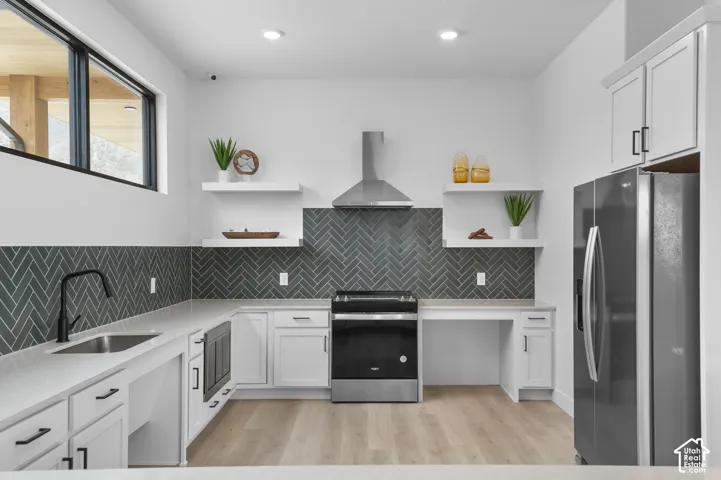 Modern kitchen featuring sleek stainless steel appliances, white cabinetry with black hardware, a herringbone pattern backsplash, light wood-finish flooring, and white countertops