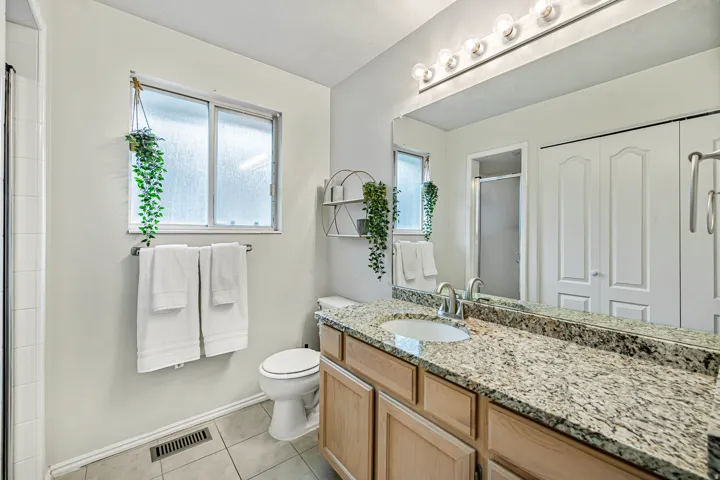 Bathroom featuring a vanity with a light-toned granite countertop and an integrated sink, a large wall-mounted mirror, and a multi-bulb light fixture